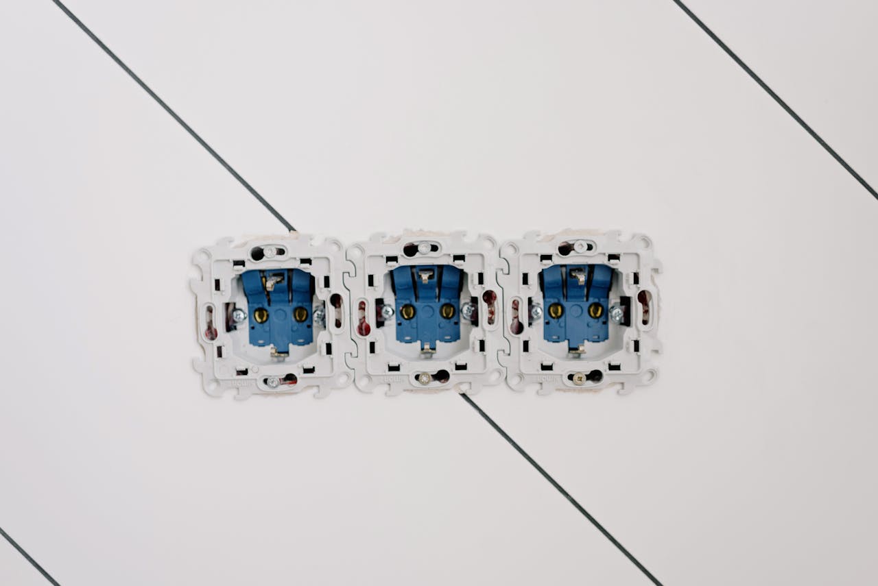 Close-up view of three blue electrical sockets installed in a white wall, showing details of wiring and connections.